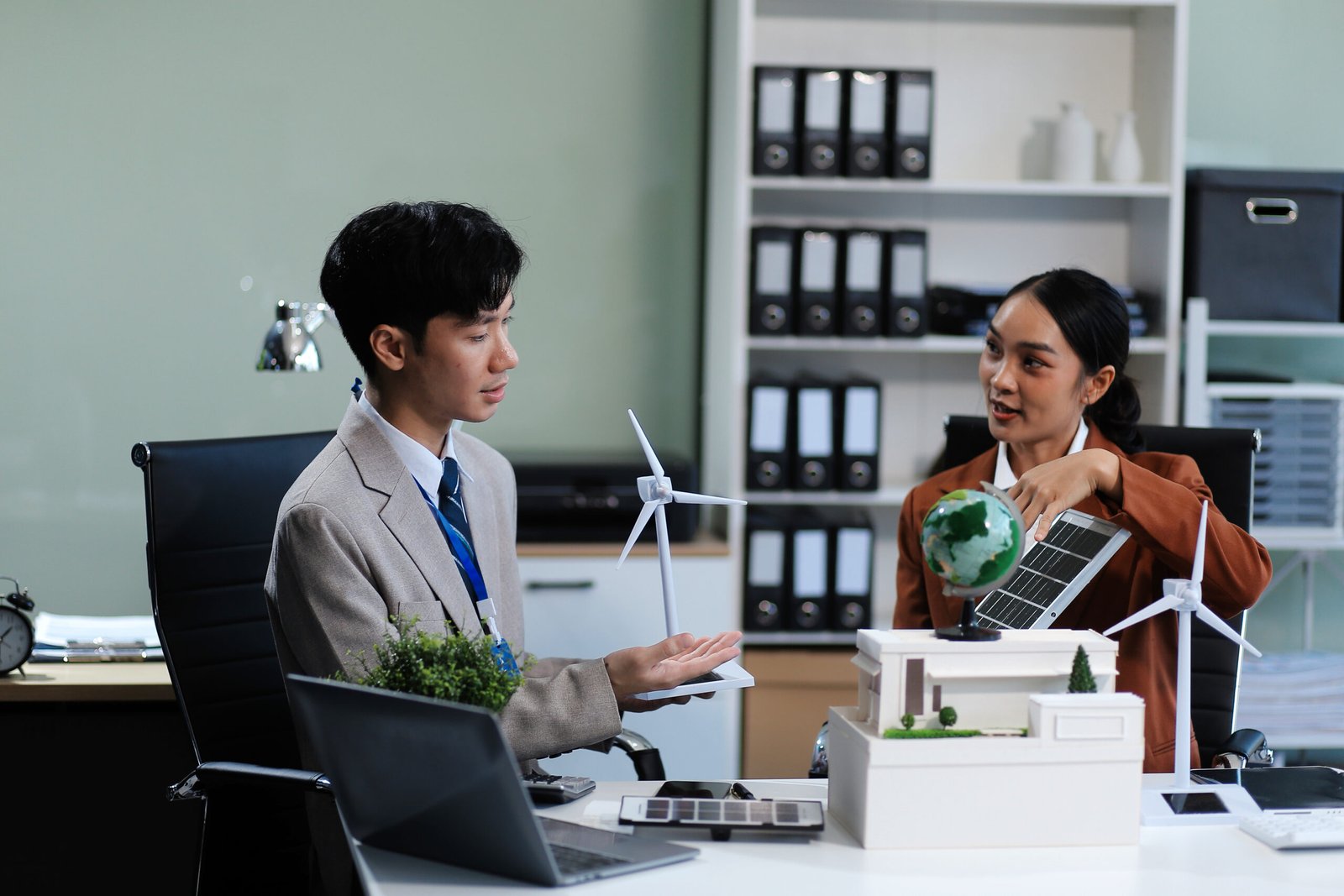 female alternative energy engineer hold a windmill power sample model and discuss with her male colleague for alternative power in the studio