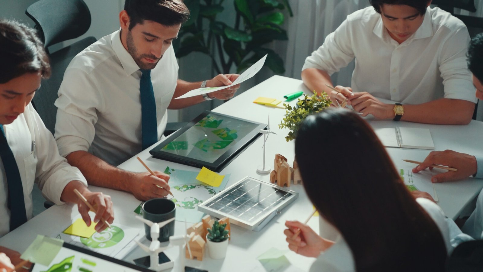 Professional smart business team discussing about using clean energy and sustainable investment at meeting table with wind mill, document with environmental graph and wooden house model. Alimentation.