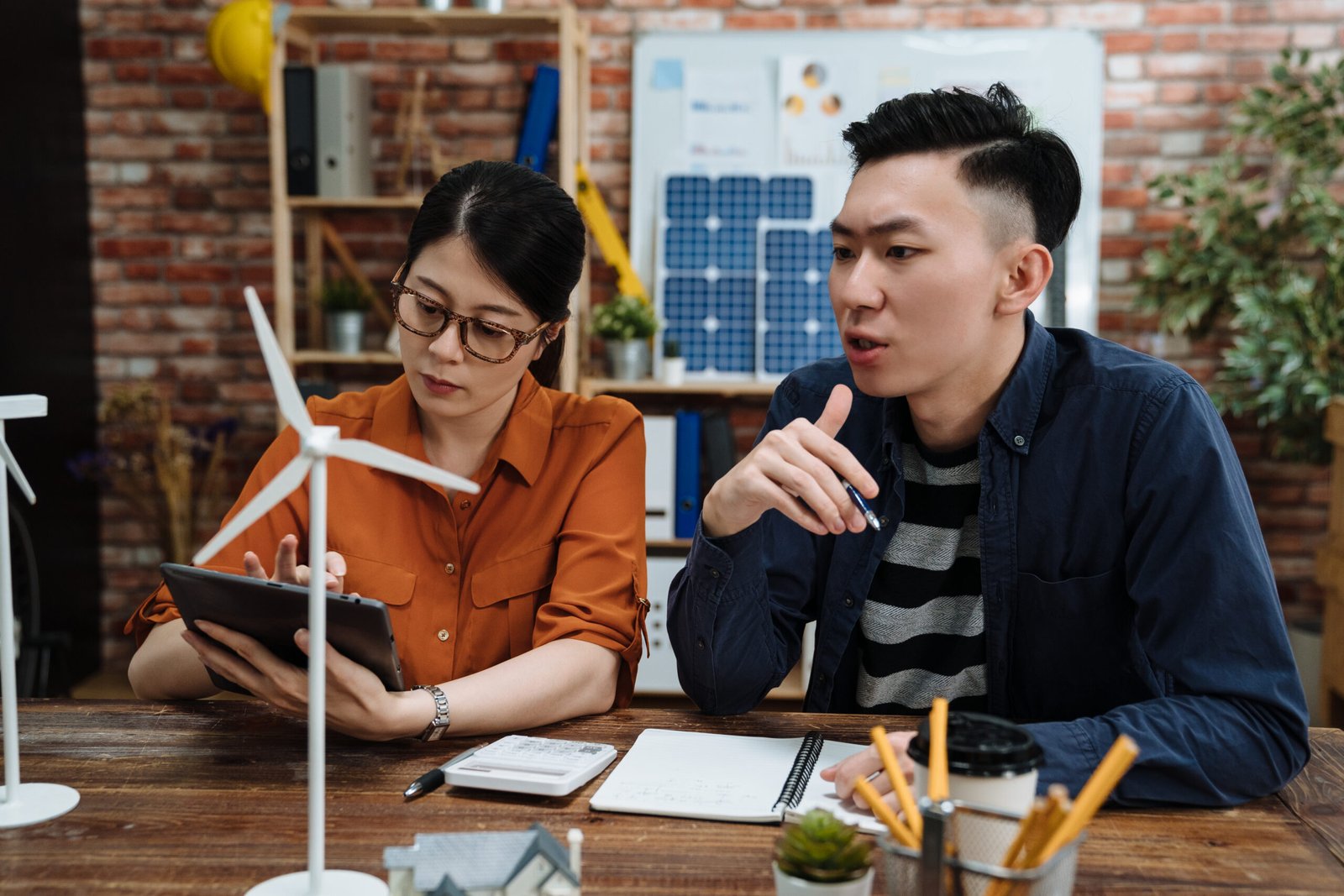 Alternative energy. concentrated two female and male colleagues designing windmills at wooden table in eco friendly company. young asian man and woman coworkers discussing renewable power project.